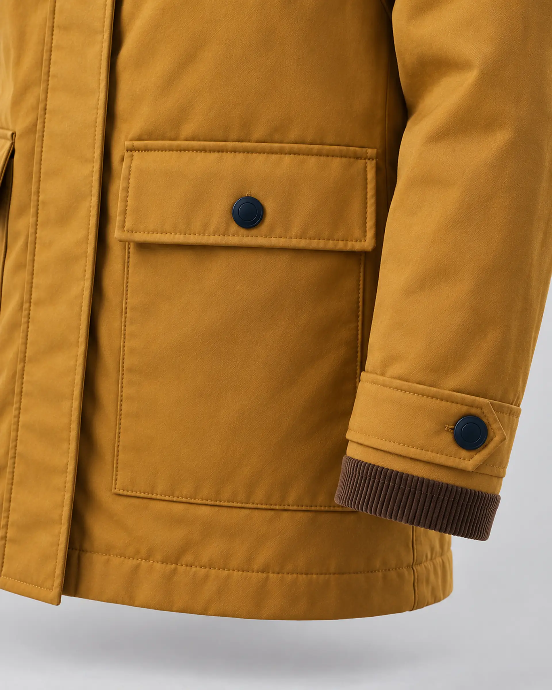 détail d’une poche et d’un poignet à bouton sur une veste ocre
